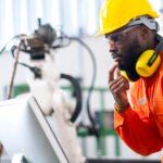 portrait of native american engineer technician wearing safty uniform hand contril automation robot arm welding machine with laptop industrial 4.0 factory background concept